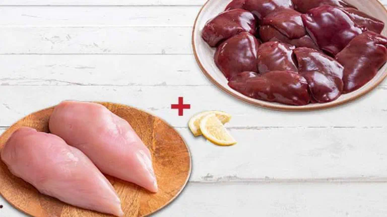 Ức gà tươi trên thớt gỗ và đĩa gan gà, kèm gừng, tỏi và chanh