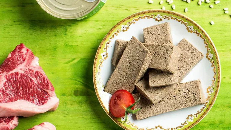 Đĩa pate cắt lát đặt cạnh hộp thiếc mở nắp và hai miếng thịt bò sống