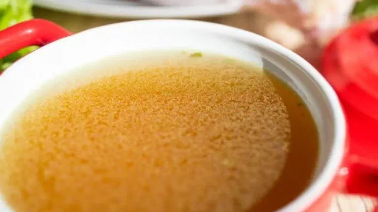 Bát sứ đựng nước dùng gà trong màu vàng nhạt, phía sau là thịt gà và cà chua